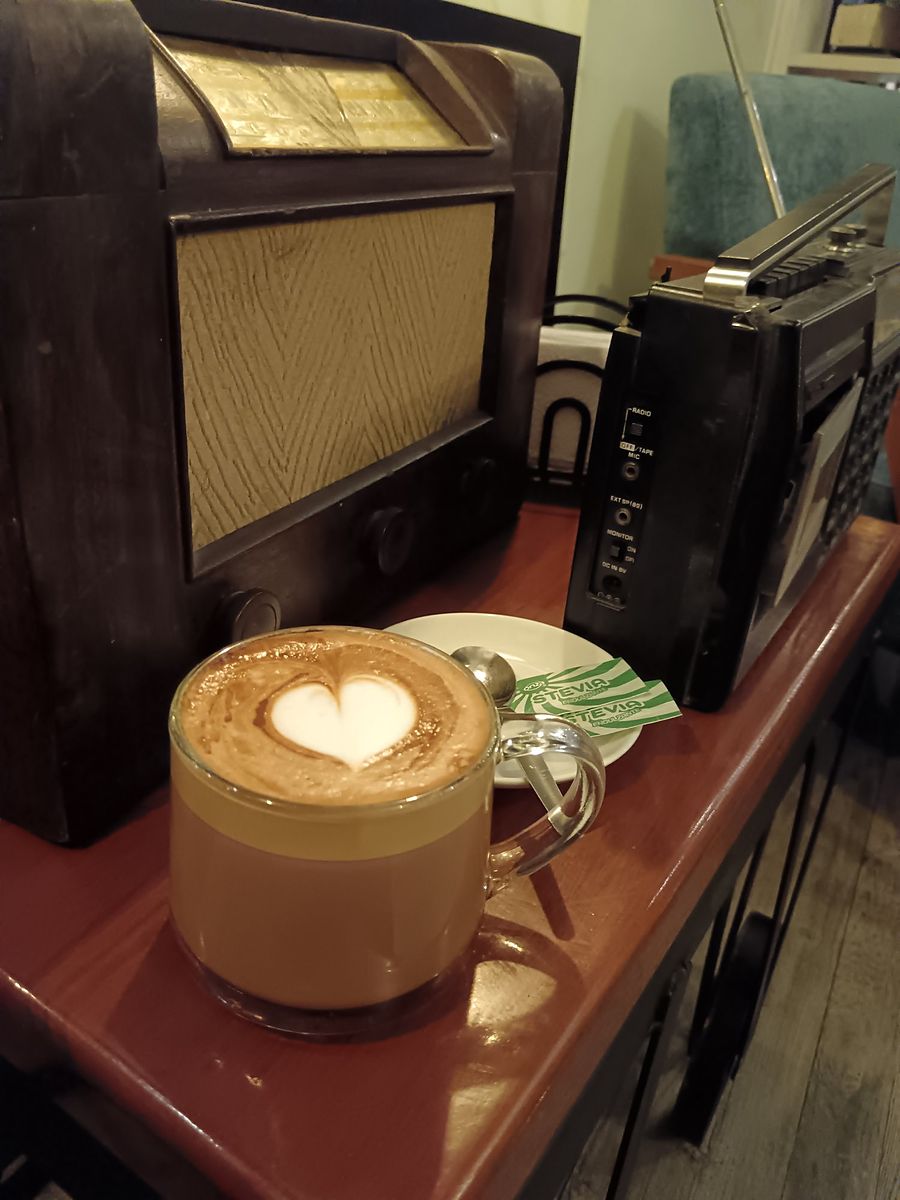 Café latte con arte de corazón junto a una radio antigua