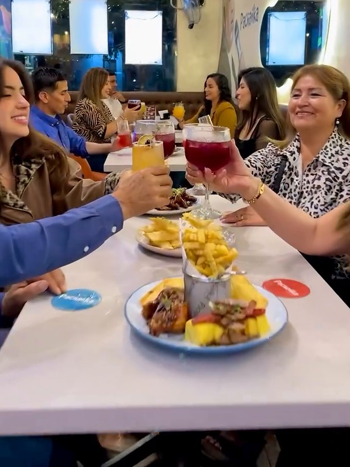 Mesa larga con varios comensales brindando y piqueos al centro